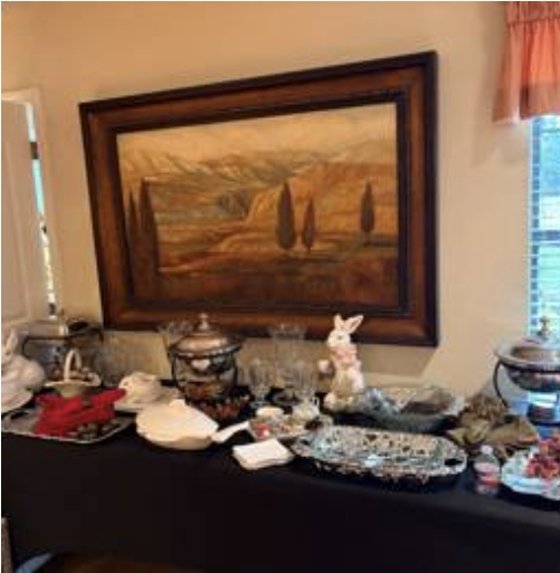 Framed landscape painting above a buffet of silver and china